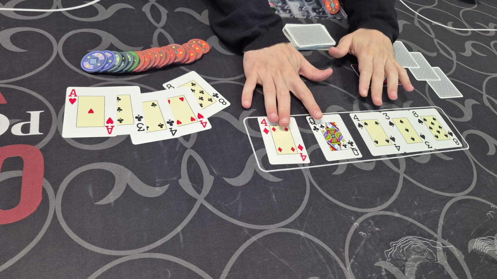 As mãos do dealer sobre o board, com uma mão de cinco cartas aberta ao lado