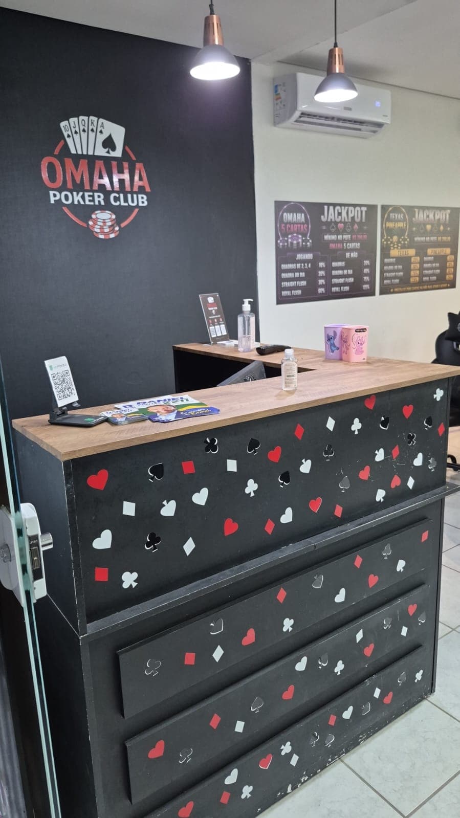 Recepção com a logo do clube pintada na parede preta e os quadros de jackpot
